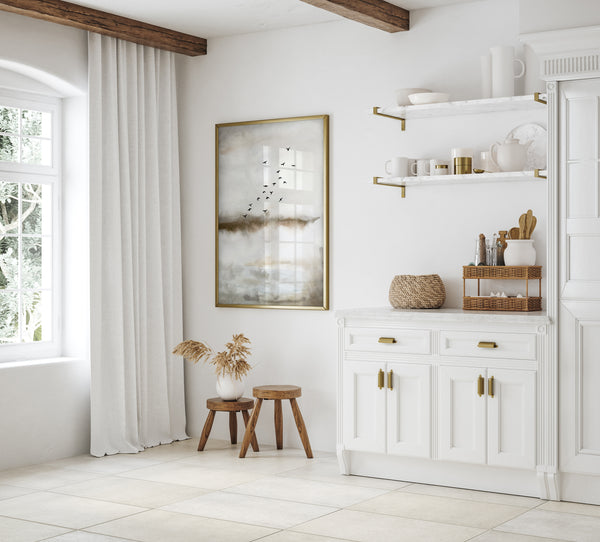 A framed watercolor painting depicting a flock of birds flying over a misty landscape. The painting is displayed on a white wall in a kitchen setting, adding a touch of nature and tranquility to the space. The kitchen features white cabinetry, a large window with sheer curtains, and a rustic wooden beam ceiling, creating a warm and inviting atmosphere.