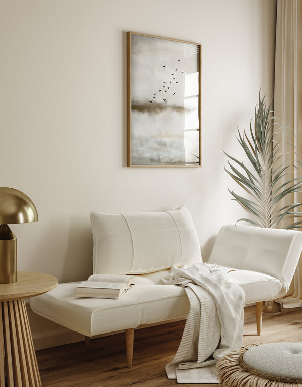 A framed watercolor painting depicting a flock of birds flying over a misty landscape. The painting is displayed on a neutral-toned wall above a cozy daybed with a soft blanket and pillows. The room is filled with natural light, creating a warm and inviting atmosphere.