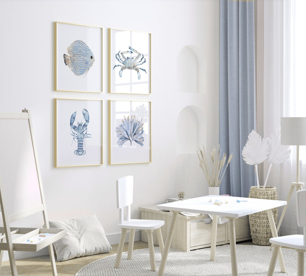 A set of four framed watercolor prints depicting coastal marine life. The prints feature minimalist designs of a discus fish, a crab, a lobster, and seaweed, all rendered in soft blues and grays. The prints are displayed on a wall in a child's bedroom or playroom, adding a touch of coastal charm to the space.