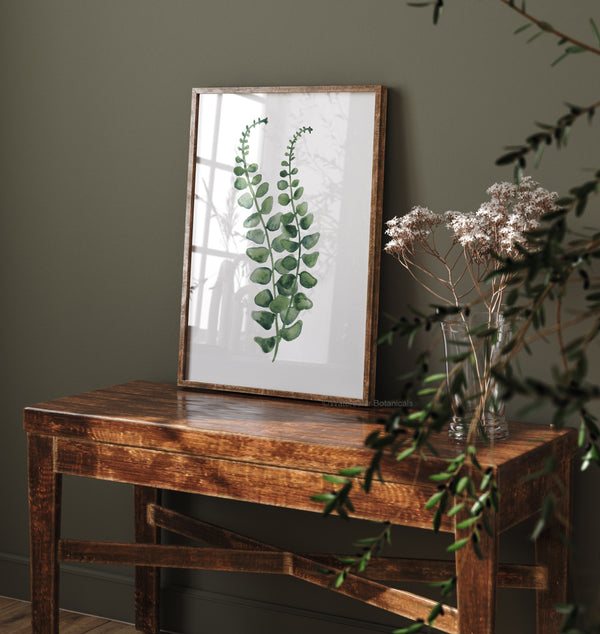 A watercolor painting of a green fern branch adds a touch of natural color to a room with a dark green wall and a wooden table.