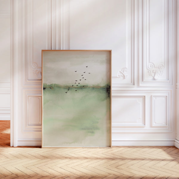 A watercolor painting of an abstract landscape in soft sage green tones with flying birds adds a touch of nature to a room with a wood floor, ornate molding, and white walls.