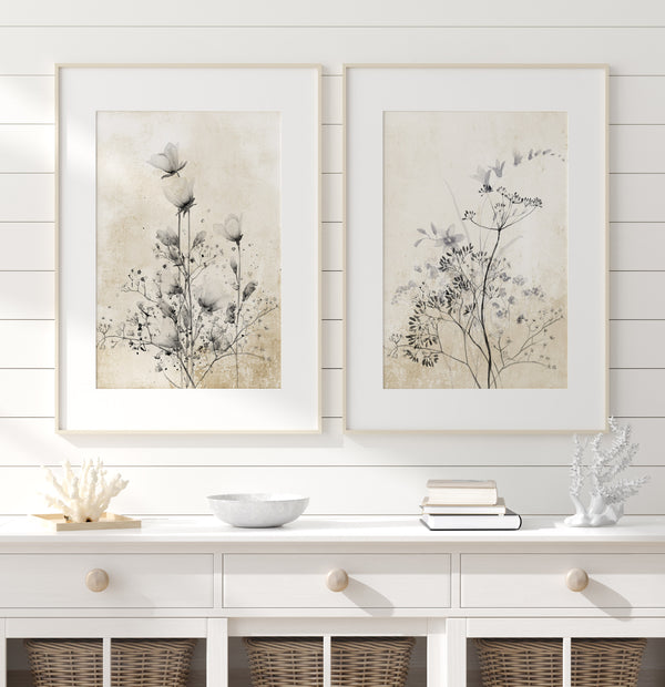 A pair of framed botanical prints featuring delicate black roses and other flowers in shades of grey and white hang above a white dresser in a coastal-inspired room.