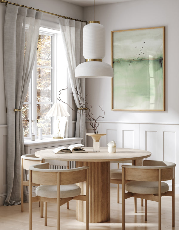 A watercolor painting of an abstract landscape in soft sage green tones adds a touch of nature to a dining room with a round table, white chairs, and gray curtains.