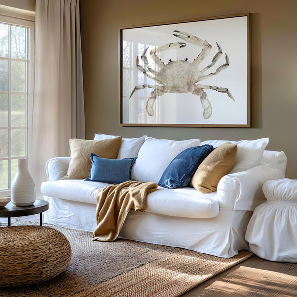 A cozy living room with a large white sofa adorned with colorful pillows and a warm throw blanket. A framed watercolor painting of a realistic crab in soft, earthy brown tones hangs above the sofa, adding a touch of coastal charm to the space.