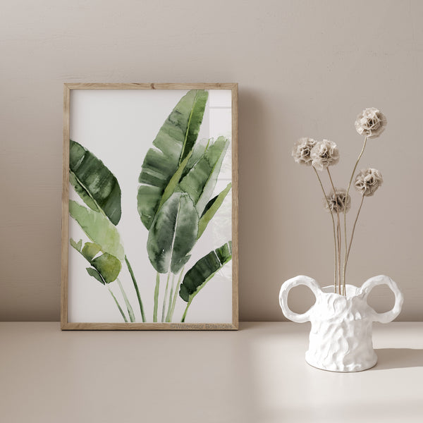 A watercolor painting of large green tropical banana leaves adds a touch of nature to a room with a light-colored wall and a white vase with dried flowers.