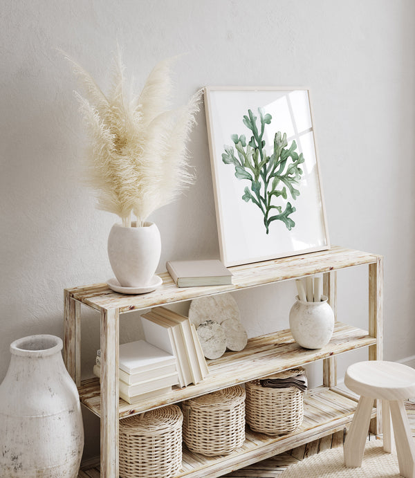 A framed watercolor painting showcases the intricate details of seaweed, creating a serene and inviting atmosphere in a space with a console table, a vase of pampas grass, and decorative accents.