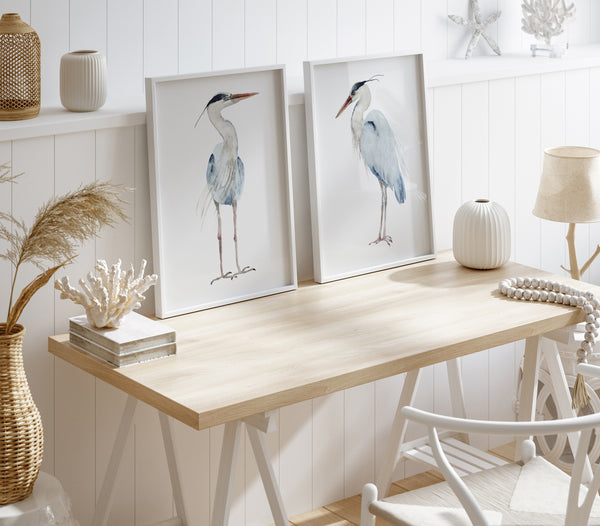 Watercolor paintings of minimalist large herons add a touch of nature to a room with a wooden desk, white paneling, and a white chair.