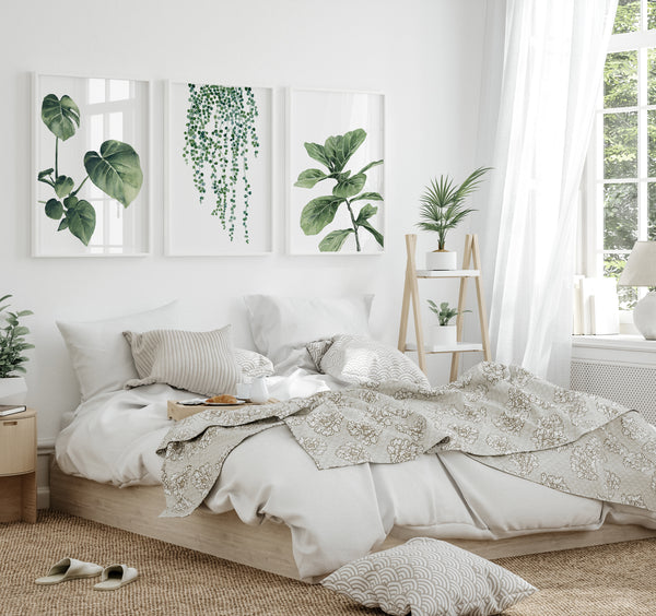 Watercolor paintings of various green tropical leaves add a touch of nature to a bedroom with a bed, a nightstand, and a plant in a corner.