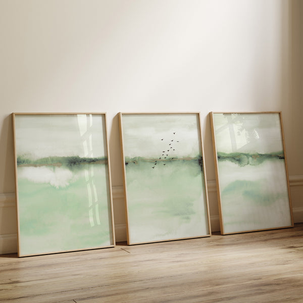 Watercolor paintings of abstract landscapes in soft sage green tones add a touch of nature to a room with a wood floor and white walls.