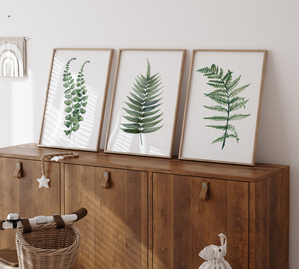 Three framed botanical prints with green leaf illustrations displayed on a wooden cabinet in a bright, modern room.