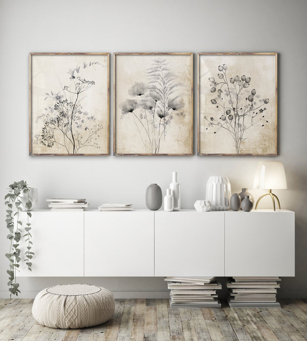 A set of three framed botanical elements showcasing delicate flowers and foliage in shades of gray and white. The prints are arranged in a row above a console table in a modern living room, adding a touch of nature and elegance to the space.