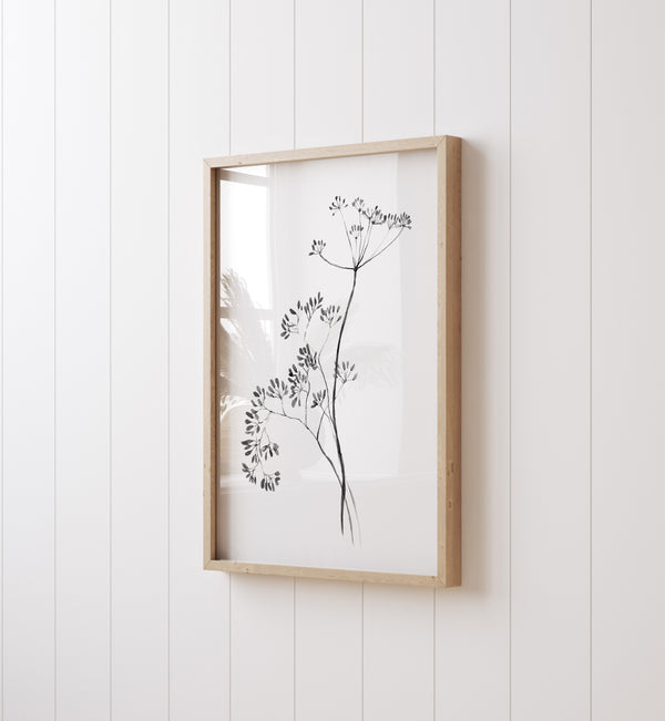 A framed black and white watercolor print showcases a delicate arrangement of flowers and branches, creating a simple yet elegant display against a white wall