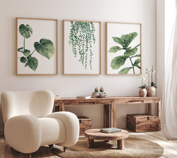 Watercolor paintings of various green tropical leaves add a touch of nature to a living room with a white armchair, a wooden table, and a round coffee table.