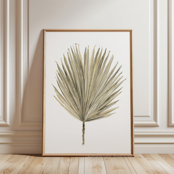 A watercolor painting of a single palmetto leaf, framed in a natural wood frame and displayed on a white wall with ornate molding. The floor is a light-colored wood with a herringbone pattern.