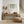 A watercolor painting of hanging green leaves adds a touch of nature to an entryway with a wooden console table, a woven pouf, and dried pampas grass in vases.