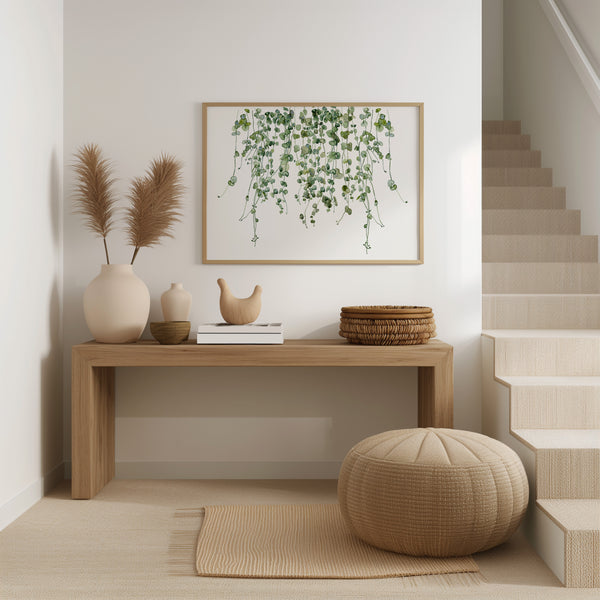 A watercolor painting of hanging green leaves adds a touch of nature to an entryway with a wooden console table, a woven pouf, and dried pampas grass in vases.