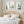 A set of three framed watercolor paintings showcasing a tall cactus, an aloe vera plant, and an opuntia cactus, displayed on a white wall above a bed in a bedroom setting. The paintings are framed in natural wood frames, complementing the warm and inviting ambiance of the room. The bedroom features a woven headboard, soft linens, and natural light, creating a serene and relaxing atmosphere. The cactus artwork adds a touch of the desert to this tranquil bedroom setting.