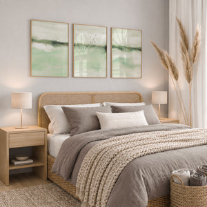 Three abstract sage green watercolor landscape prints above a bed in a calm, neutral bedroom