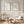 Two framed botanical art prints with black line drawings on white backgrounds, hung on a cream paneled wall above a light wood chair and a round wooden coffee table in a styled interior.