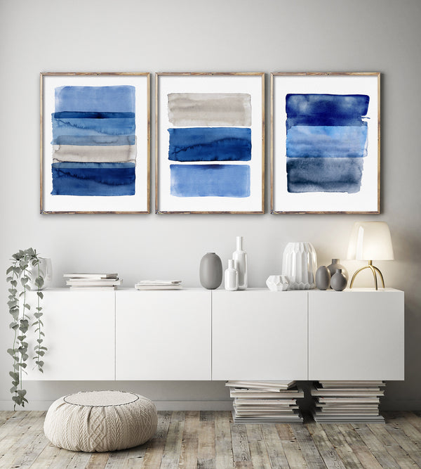 Three framed abstract blue artworks on a wall above a white console table.