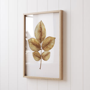 minimalist yellow autumn leaf painting hangs in wooden frame viewed from an angled perspective 