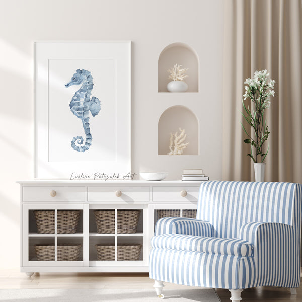 Blue watercolor seahorse print in a white frame on a white sideboard, next to a blue and white striped armchair