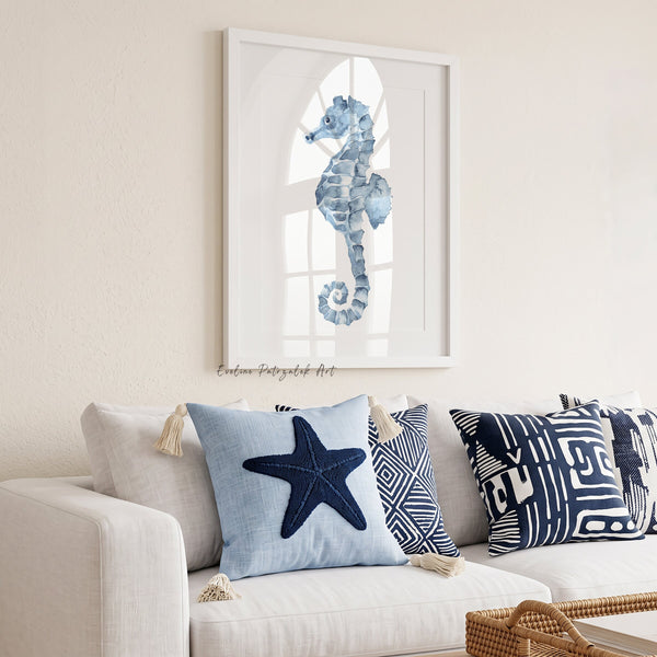 Framed blue seahorse watercolor print above a white sofa with navy and light blue cushions