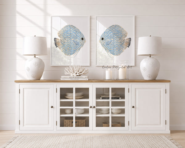 White sideboard with glass doors, two framed artworks of fish, and two white lamps in a room with light wood flooring.