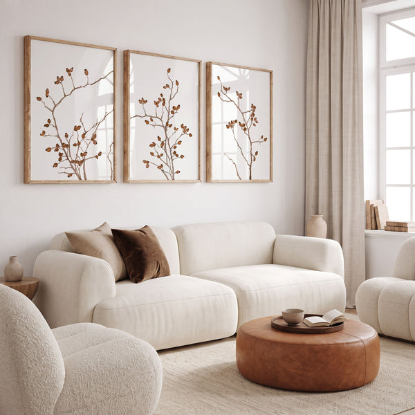 Three cognac brown botanical prints of berry branches above a cream sofa with a leather pouf
