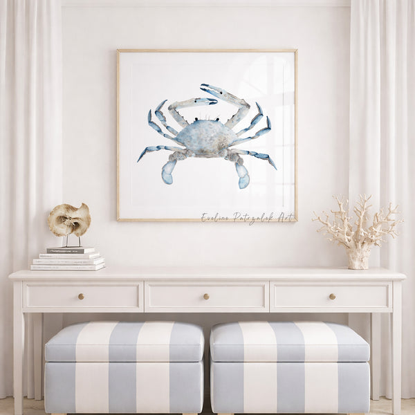 Framed artwork of a blue crab on a wall above a white console table with striped stools.
