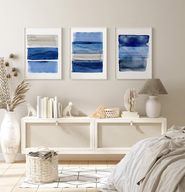 Three abstract blue artworks on a wall above a white console table with decorative items.