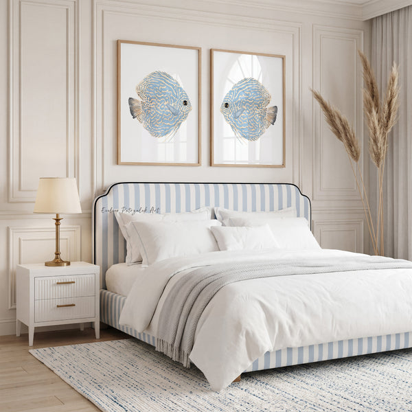 Blue discus fish watercolor wall art set of two displayed above a bed in a bright blue and white coastal bedroom with natural wood frames.