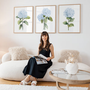 Watercolor artist Eveline Patrzalek on a sofa beneath her three blue hydrangea watercolor prints