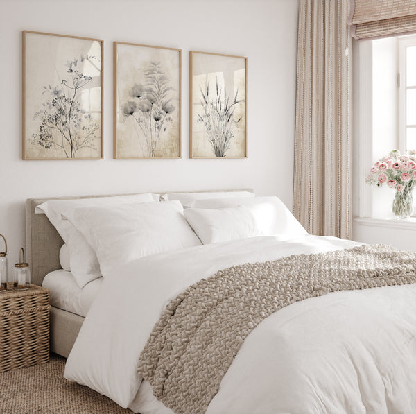 Three framed prints showcasing delicate botanical designs in muted colors, creating a calming and elegant atmosphere above a bed in a serene bedroom.