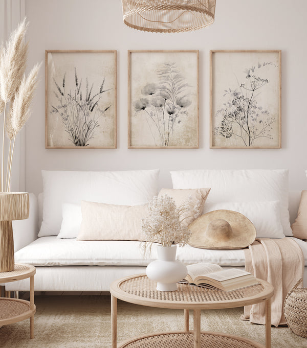 Three framed prints showcasing delicate botanical designs in muted colors, creating a calming and elegant atmosphere above a sofa in a living room with natural decor.