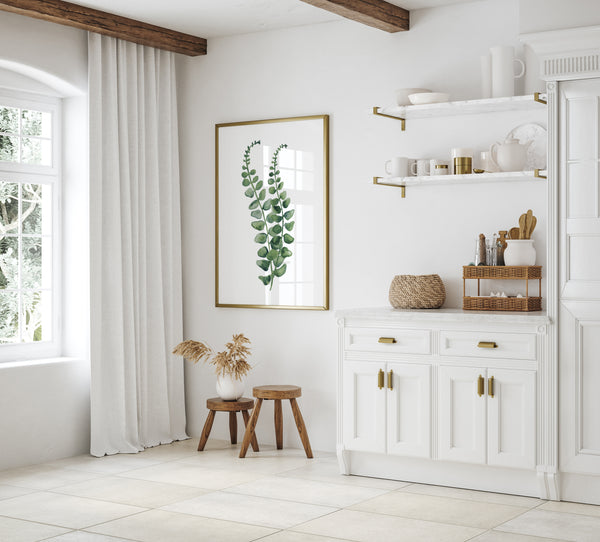 A watercolor painting of a green fern branch adds a touch of nature to a kitchen with white cabinets, a wooden ceiling, and a white marble countertop.