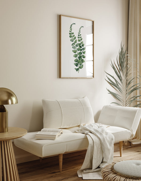 A watercolor painting of a green fern branch adds a touch of nature to a living room with a white daybed, a round side table, and a gold lamp.