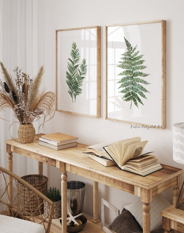 Two green watercolor prints of palm fronds and a fern above a wooden console with dried flowers