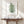 Green fern botanical print on a white brick wall above a console with white vases