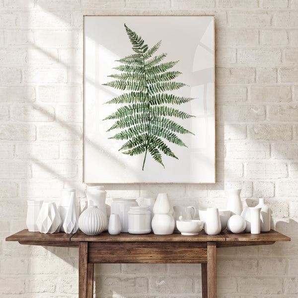 Green fern botanical print on a white brick wall above a console with white vases