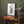 A watercolor painting of a green fern branch adds a touch of natural color to a room with a dark green wall and a wooden table.