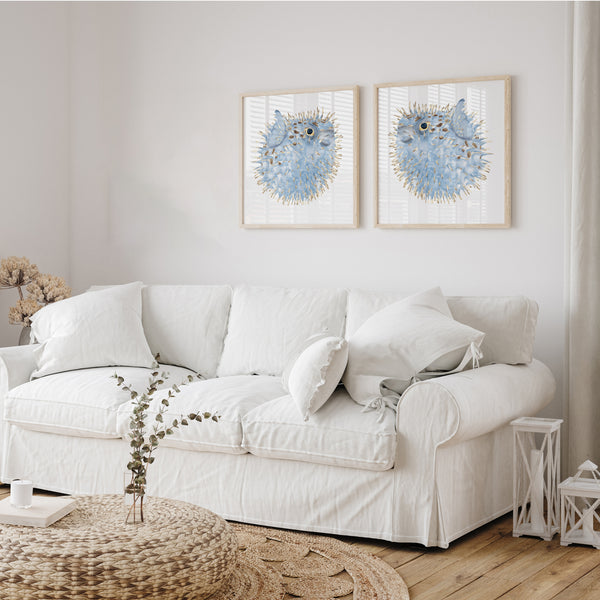 Set of 2 blue puffer fish wall art prints in wooden frames – coastal watercolour sea life artwork styled above white sofa in bright living room with natural woven coffee table and neutral decor