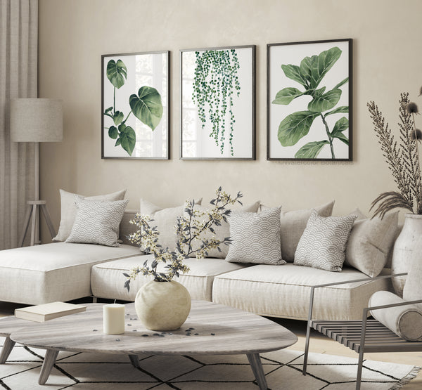 Watercolor paintings of various green tropical leaves add a touch of nature to a living room with a white sectional sofa, a round coffee table, and a floor lamp.