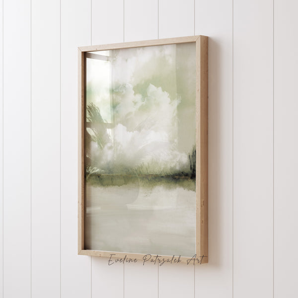 A framed art print featuring an abstract landscape with soft green and white clouds over a calm water scene, displayed on a white shiplap wall. The print is housed in a light natural wood frame, and a watermark reading 'Eveline Pietrzalek Art' is visible at the bottom.