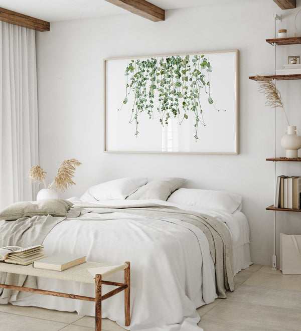 A watercolor painting of hanging green leaves adds a touch of nature to a bedroom with a bed, a wooden bench, and a shelf with books.