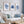 Watercolor paintings of minimalist seaweed and coral designs in deep navy blue add a touch of nature to a living room with a white couch, blue pillows, and a wooden coffee table.