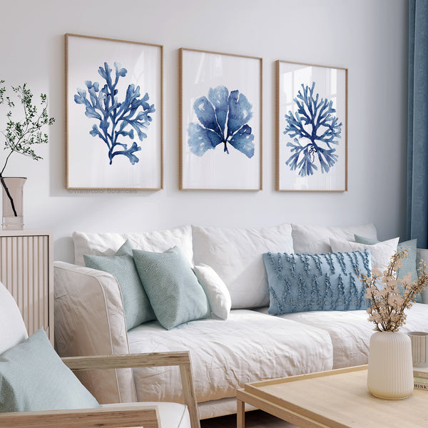 Watercolor paintings of minimalist seaweed and coral designs in deep navy blue add a touch of nature to a living room with a white couch, blue pillows, and a wooden coffee table.