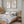 A pair of framed watercolor paintings depicting elegant great blue herons in soft neutral tones against a vintage-inspired background. The paintings are displayed on a wall above a bed in a bedroom with a serene and calming atmosphere.