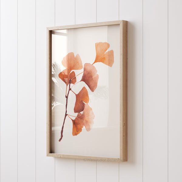 A framed watercolor botanical print featuring a delicate branch of ginkgo leaves. The leaves are rendered in warm, earthy tones against a crisp white background, giving the piece a minimalist yet elegant feel.