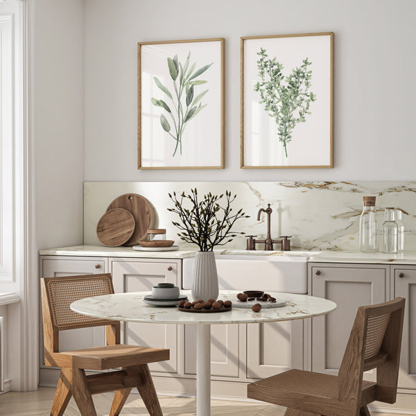 Watercolor paintings of green sage and thyme leaves add a touch of nature to a kitchen with a white marble countertop, wooden chairs, and a round dining table.